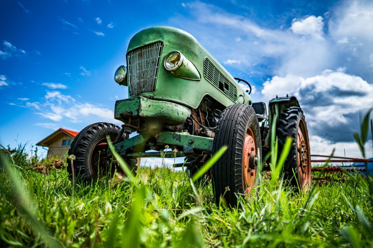 Close-up of an old green tractor in a grassy field with a blue sky.