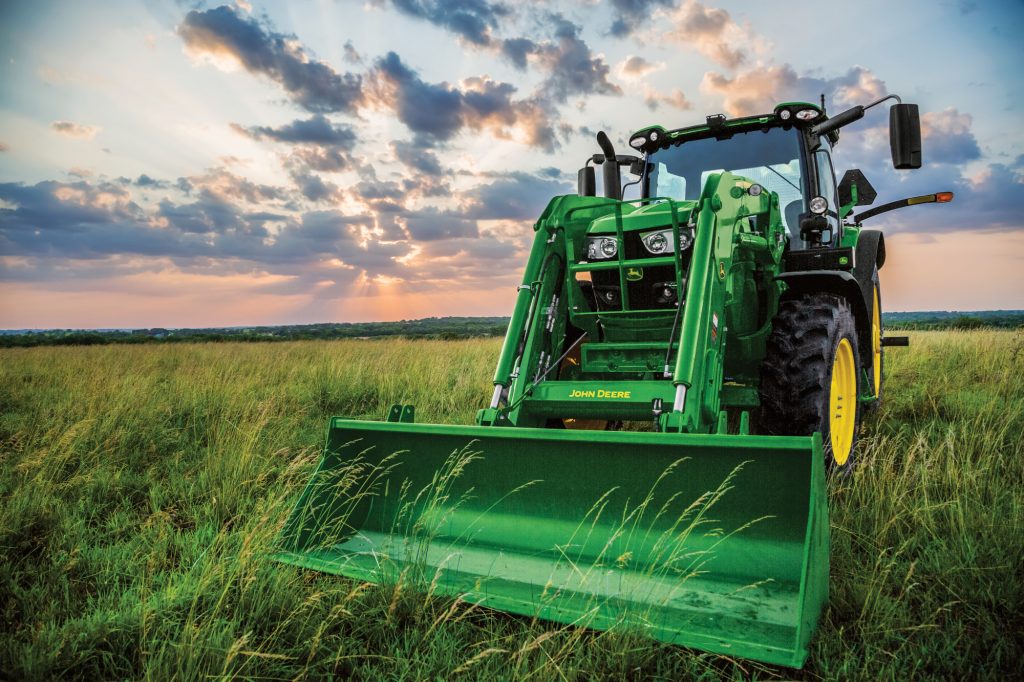 A green John Deere tractor sits in a grassy field under a dramatic sunset sky.