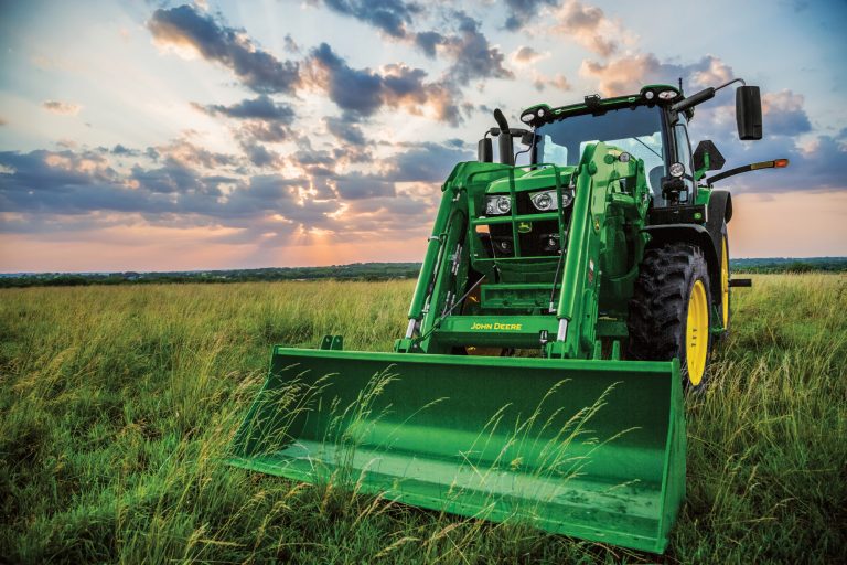 A green John Deere tractor sits in a grassy field under a dramatic sunset sky.