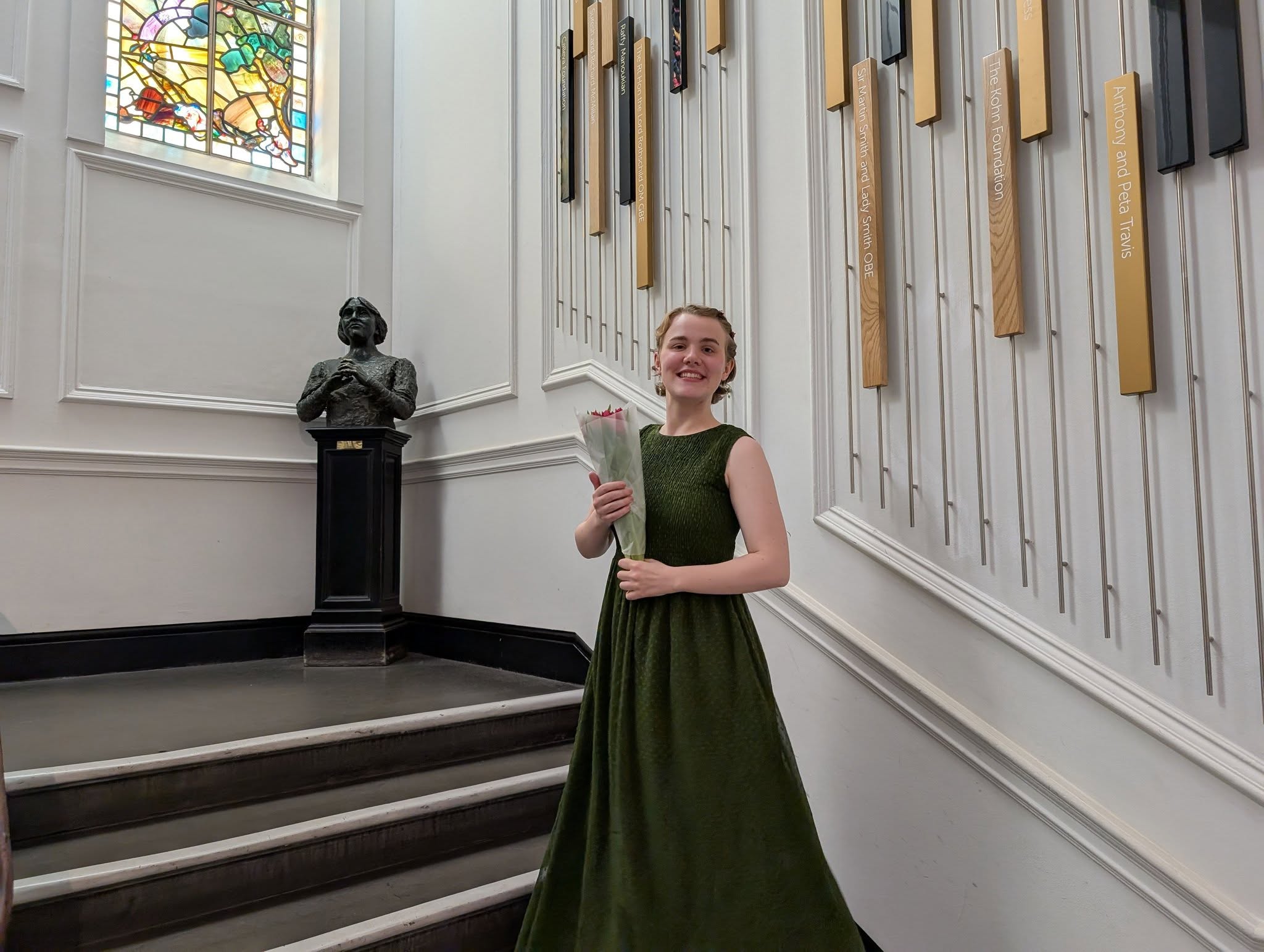 A woman in a green dress posing with flowers on a staircase