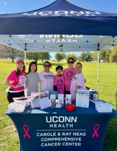 5 women and a boy stand under a tent behiind a table that says uconn health