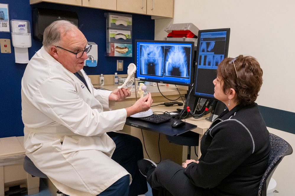 physician showing patient a model hip in an exam room