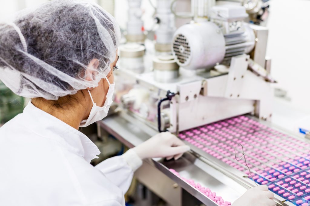 A woman in protective lab gear manufactures pink tablets.