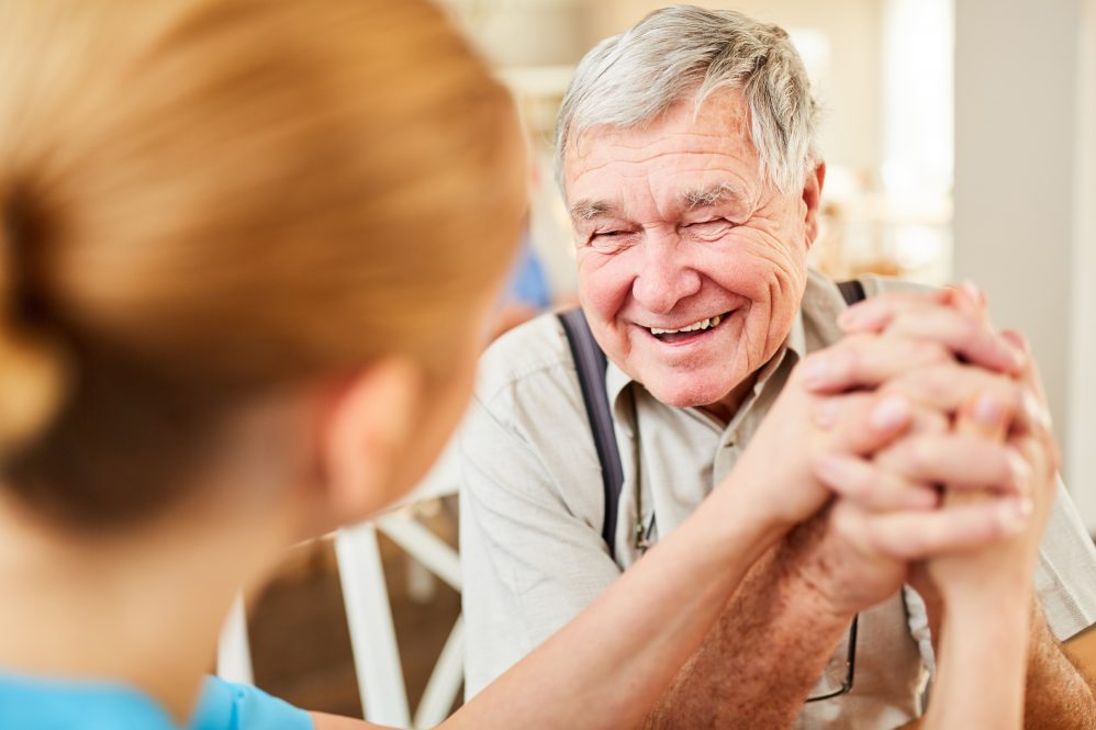 An elderly man smiles while in conversation with a younger woman.