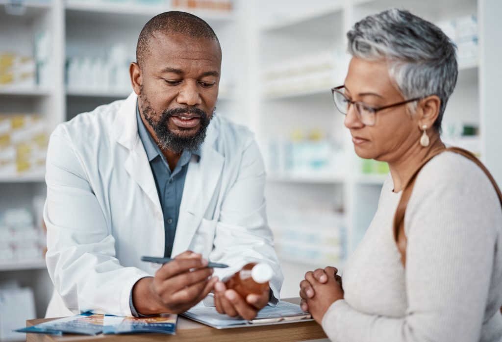 A pharmacist in a white coat examines the label on a prescription bottle with a patient.