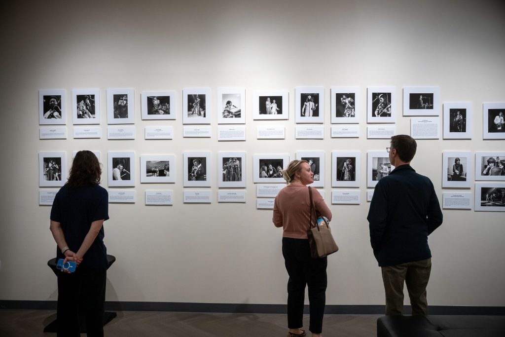 Three people look at two long lines of black and white portraits hanging on a white wall.