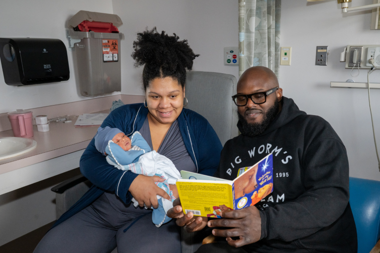 Woman and man holding new baby and reading a book to the baby
