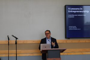 A speaker presents at a podium during a session titled 
