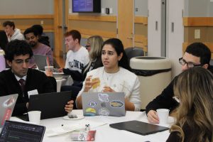 Students sit at a table discussing ideas during a collaborative workshop, with laptops and notes in front of them. 