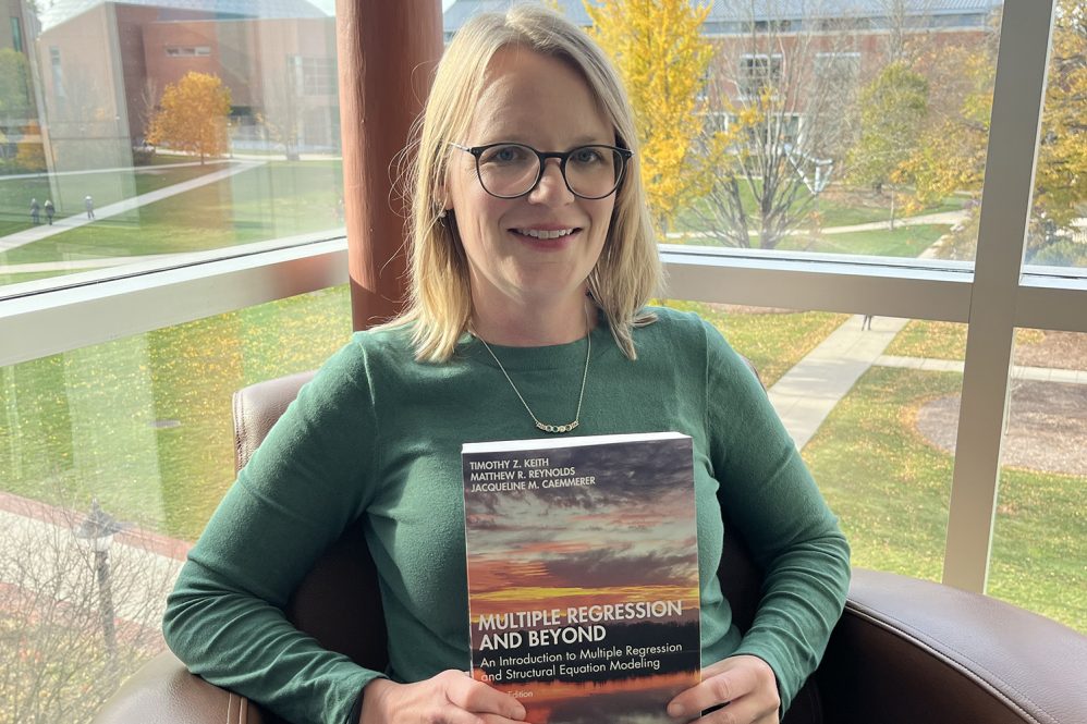 Jacqueline Caemmemer sits in a chair and holds her new book 
