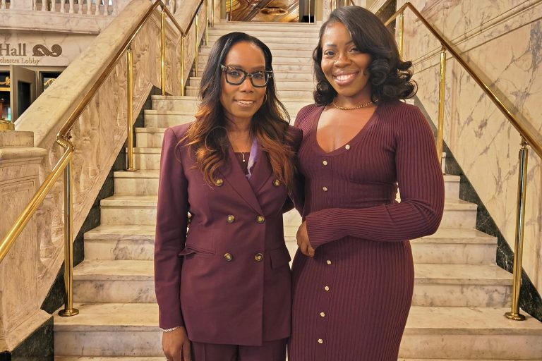 On the steps of the Waterbury Palace Theater Keynote speaker Dr. Linda Barry of UConn (left) with N. Chineye Anako of Trinity Health (right) both wearing maroon outfits and smiling.