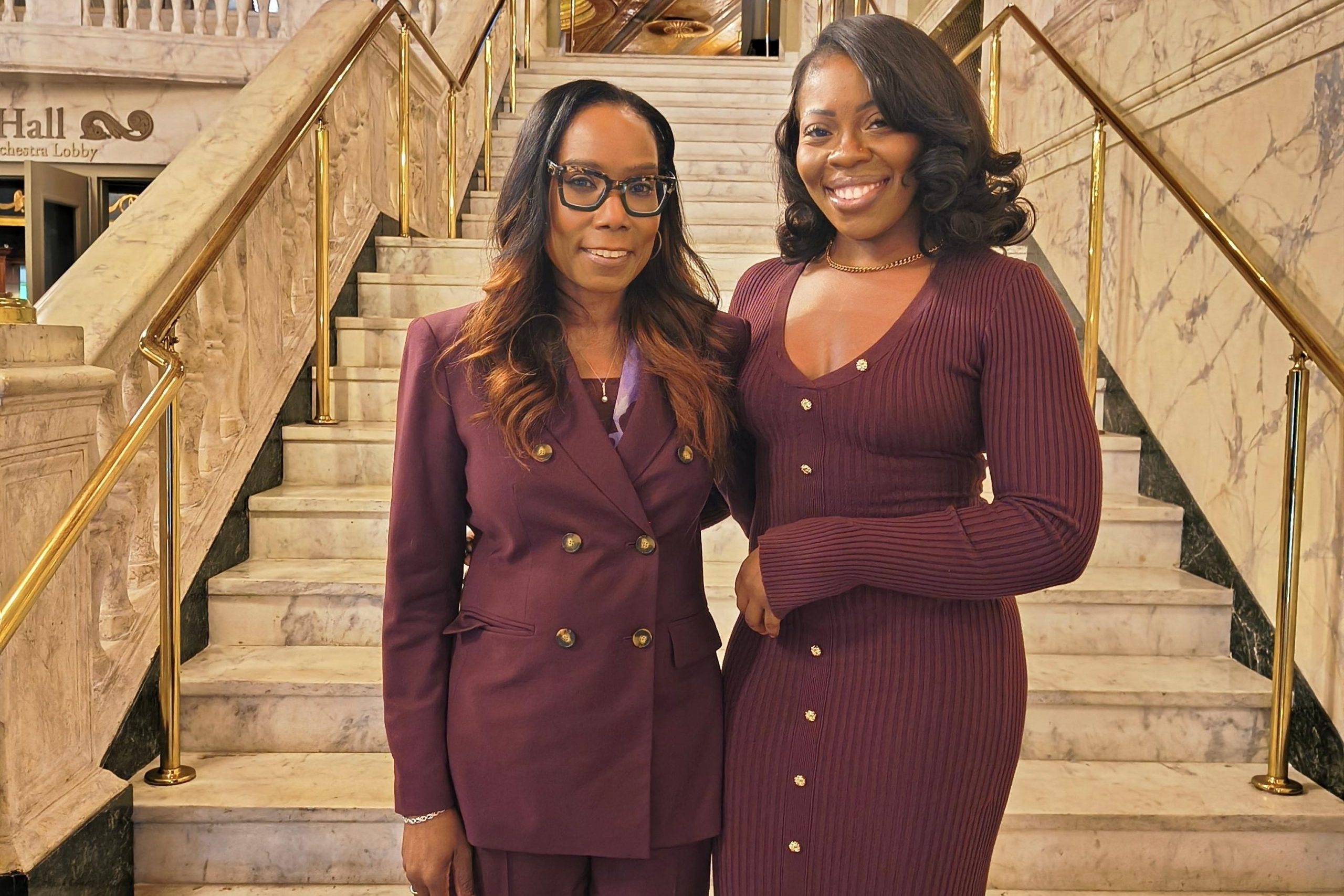 On the steps of the Waterbury Palace Theater Keynote speaker Dr. Linda Barry of UConn (left) with N. Chineye Anako of Trinity Health (right) both wearing maroon outfits and smiling.