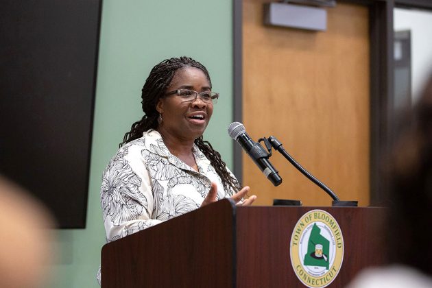 Fiona Vernal speaks and gestures at a podium featuring the Town of Bloomfield seal.