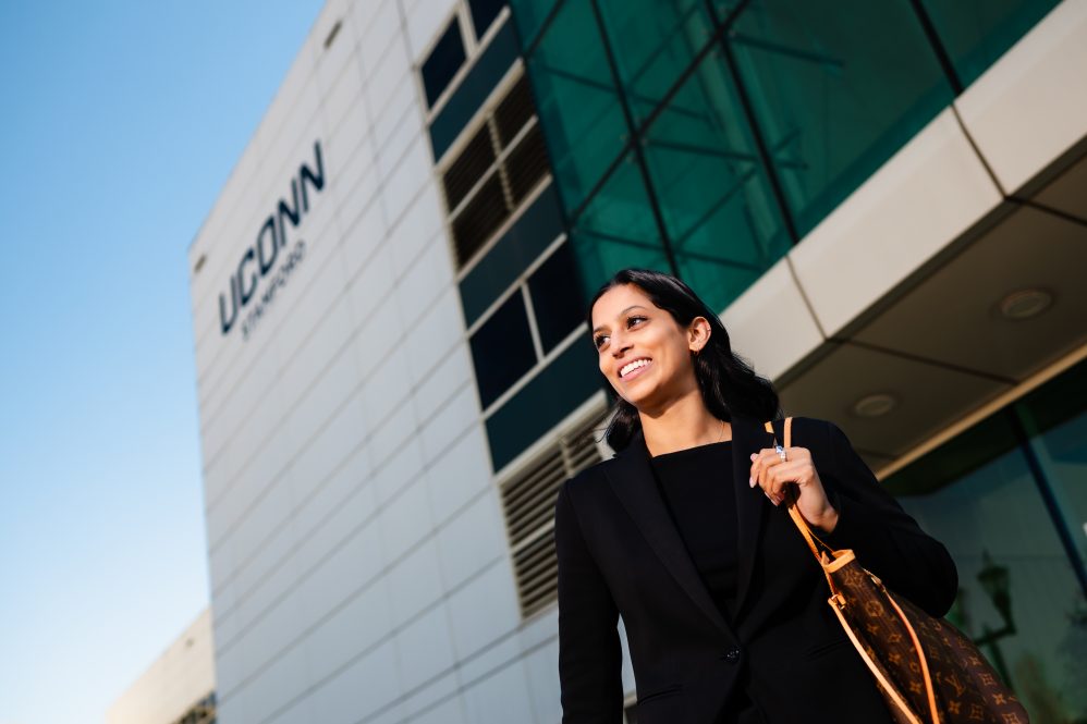 A woman stands in front of the UConn Stamford building.