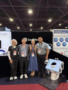 Four people wearing lanyards at a convention pose together for a photograph.