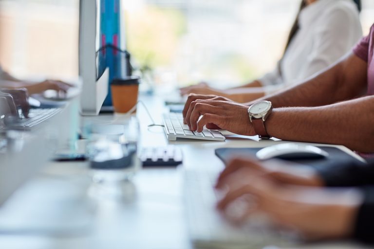 Image of human hands typing on computer keyboards in an office