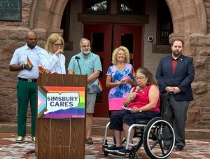 woman in wheelchair speaking into microphone with other people standing around her