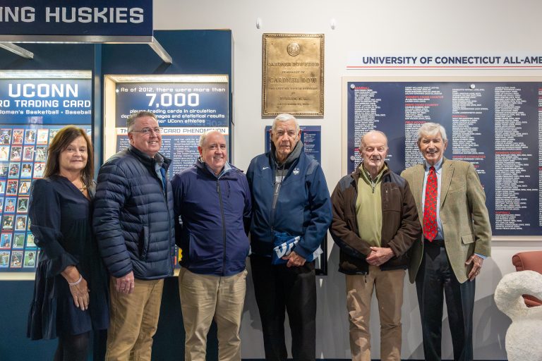 Six people standing in front of a plaque at the Husky Heritage Sports Museum