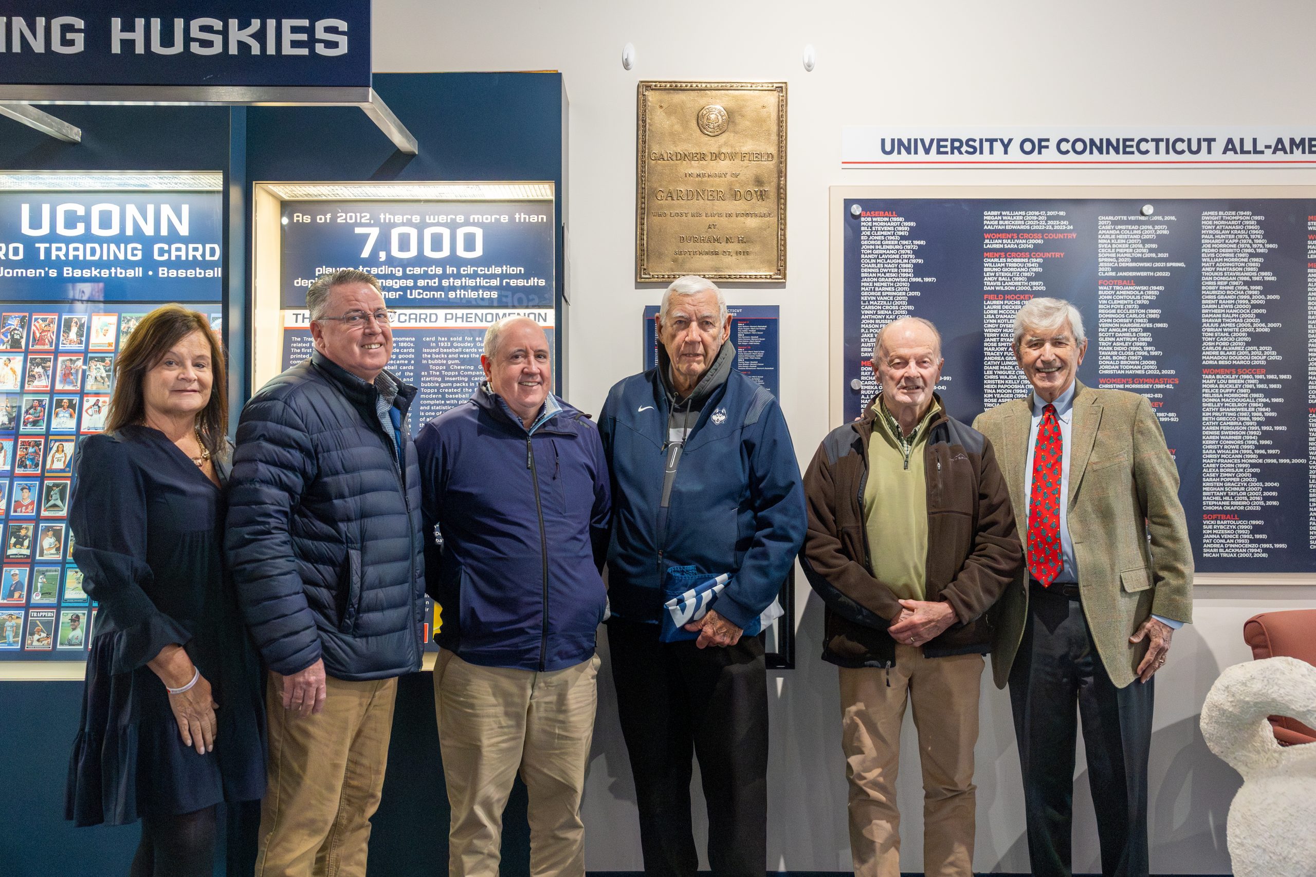 Six people standing in front of a plaque at the Husky Heritage Sports Museum
