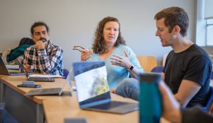 Three faculty members discuss ideas during a small group meeting in a classroom.
