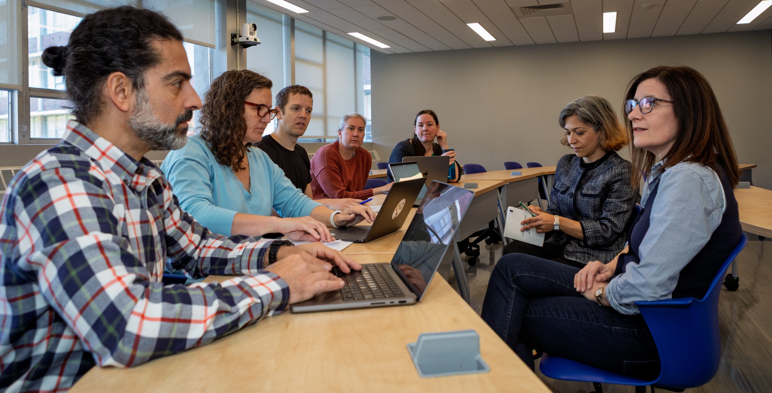 Faculty members sit around a table using laptops during a collaborative meeting.