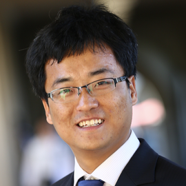 A portrait of a smiling man wearing glasses, a suit, and a tie.