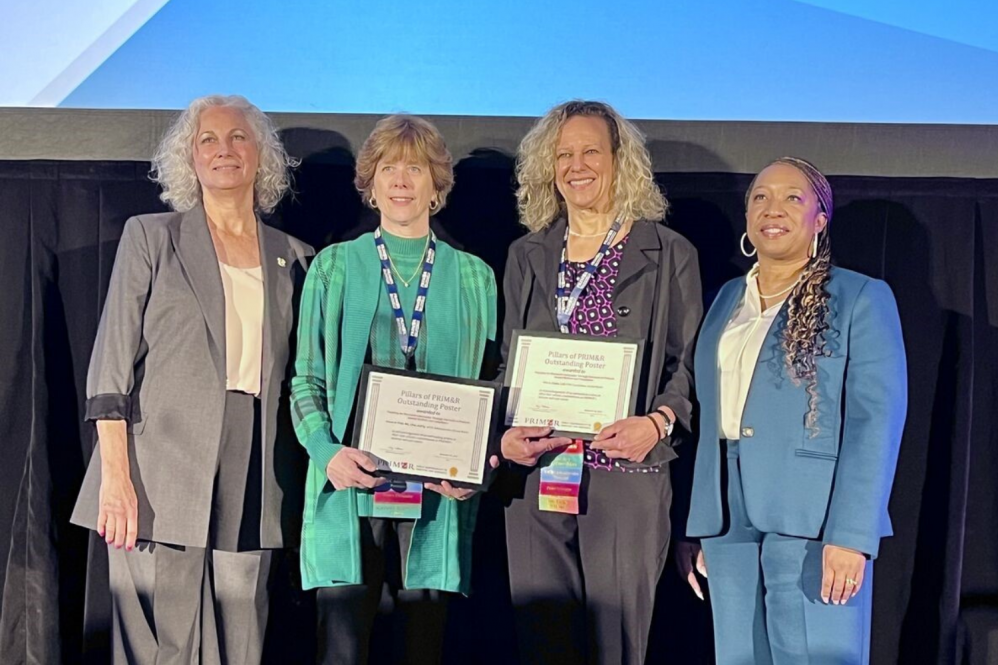 Alison D. Pohl (center left) and Lisa A. Chuba (center right) being awarded on stage and smiling holding their awards.