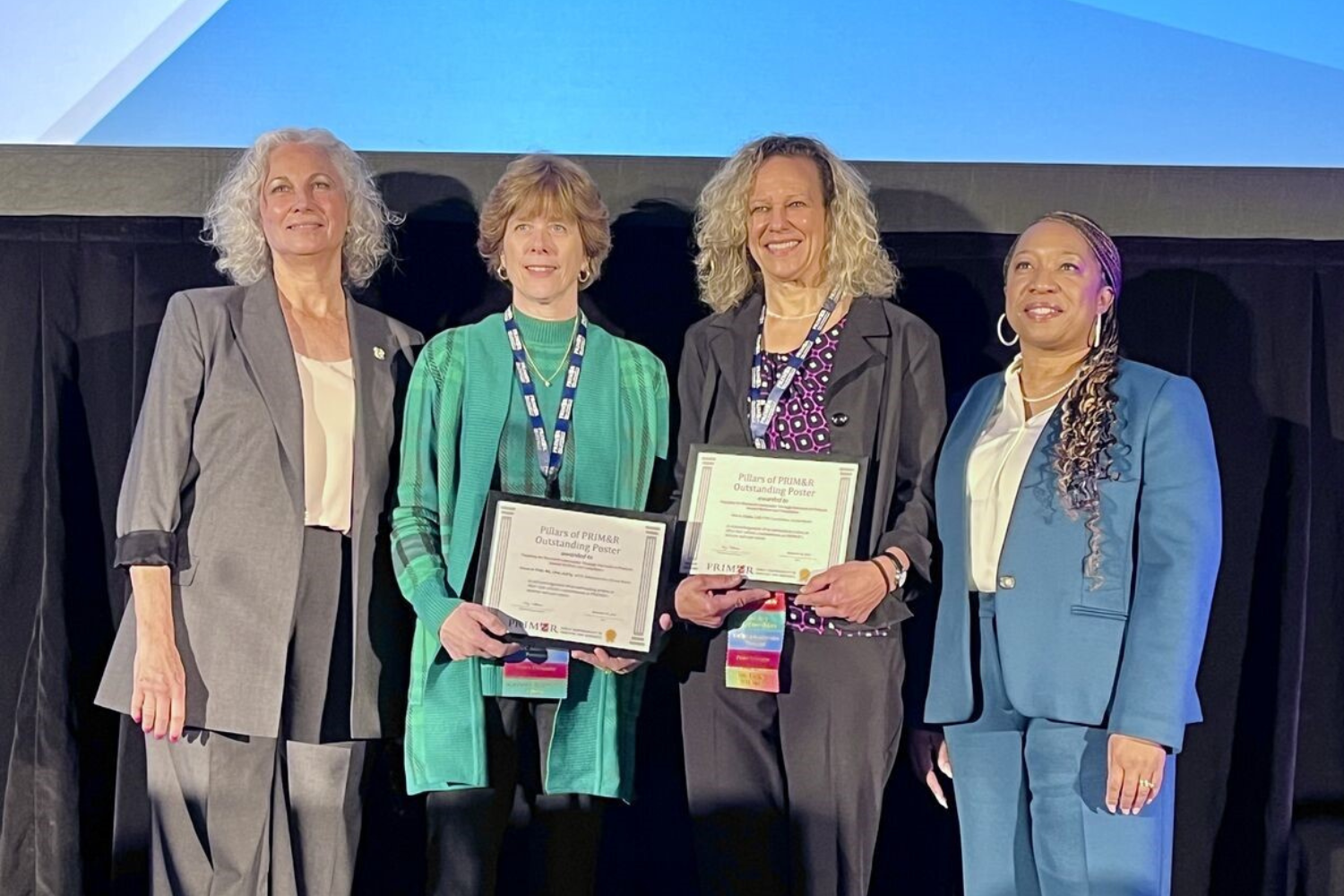Alison D. Pohl (center left) and Lisa A. Chuba (center right) being awarded on stage and smiling holding their awards.