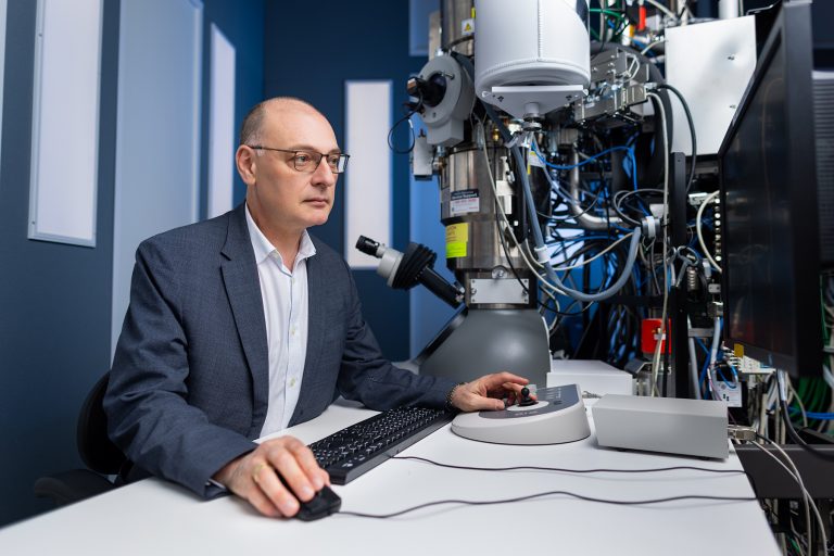 UConn interim Provost Pamir Alpay sitting next to a microscope