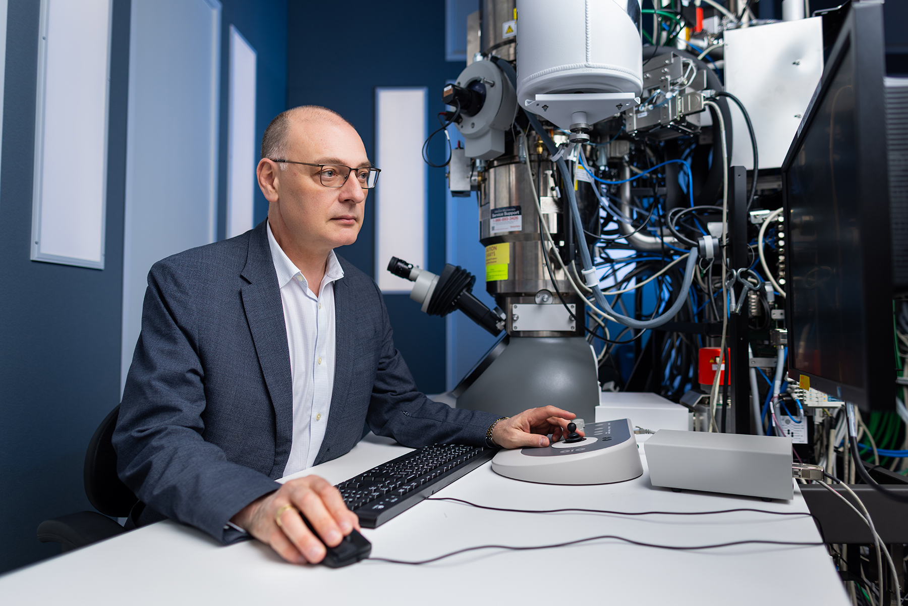 UConn interim Provost Pamir Alpay sitting next to a microscope