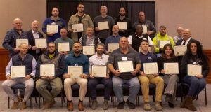A large group of Road Scholar program graduates pose together holding their completion certificates.