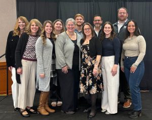 The T2 Center staff stand together smiling for a group photo in front of a black backdrop.