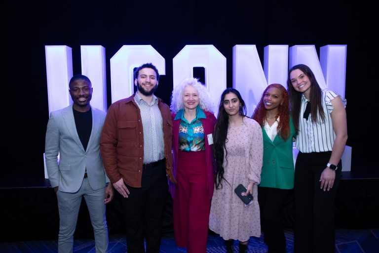 A group of people pose in front of a large UConn sign.