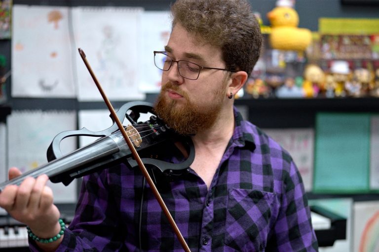 A man playing an electric violin in a purple plaid shirt