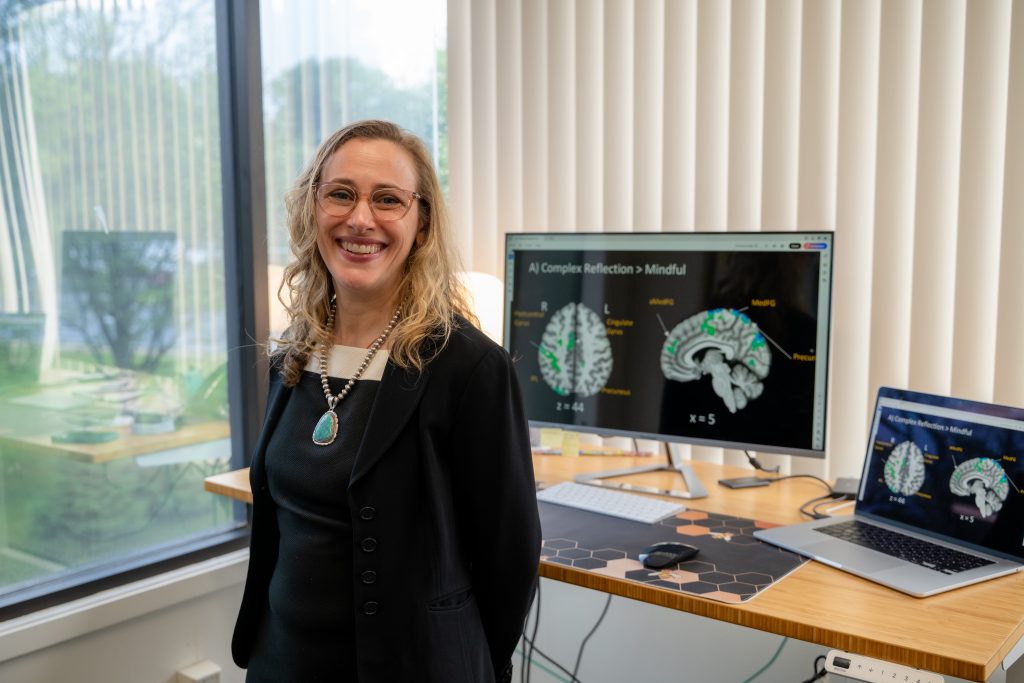 Dr. Feldstein Ewing smiling in her office with brain scans on computer.