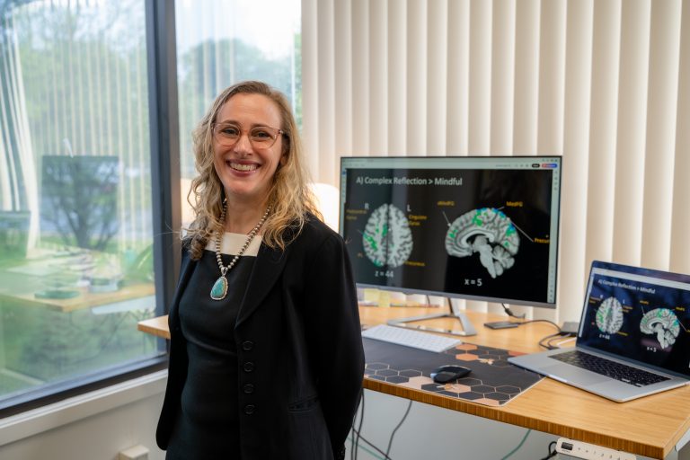 Dr. Feldstein Ewing smiling in her office with brain scans on computer.