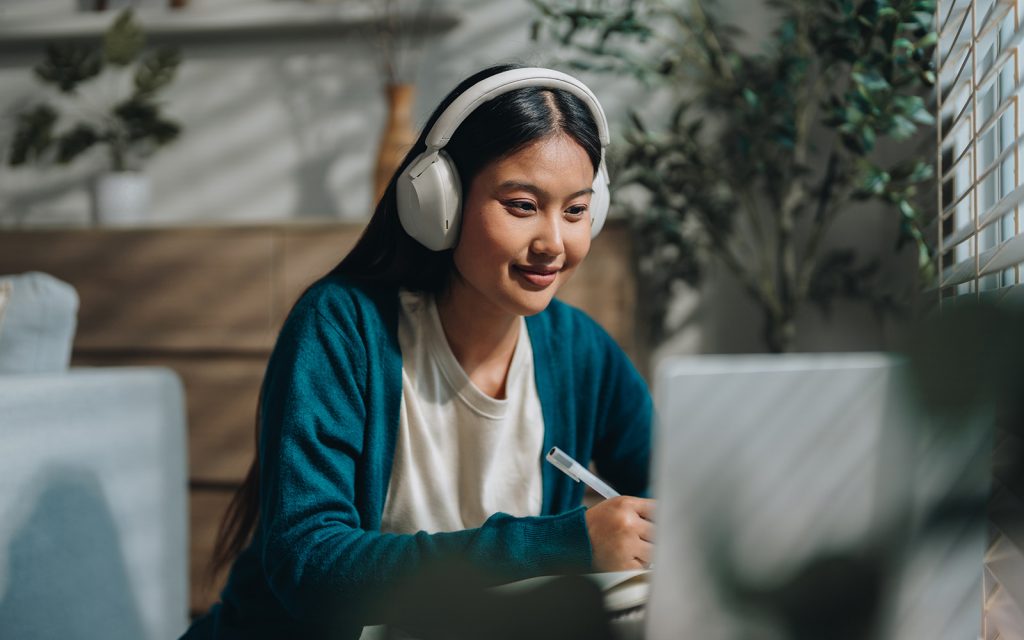 Woman enjoying her online class, attentively taking notes as she stays engaged and focused. With a sense of curiosity and dedication, she embraces the opportunity to learn from home and improve her knowledge