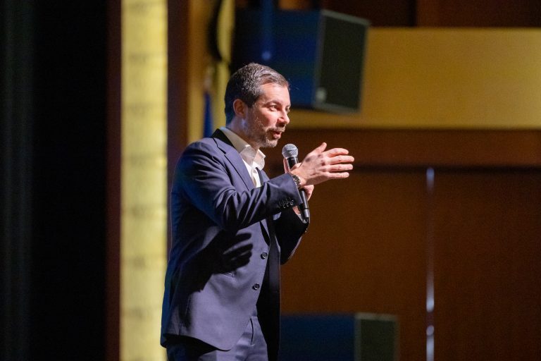 Former U.S. Transportation Secretay Pete Buttigieg gestures while holding a microphone.