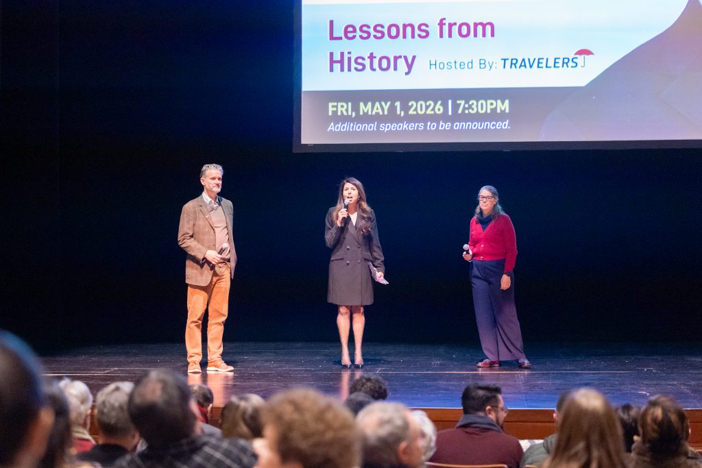 Three people stand on stage in front of a large screen.