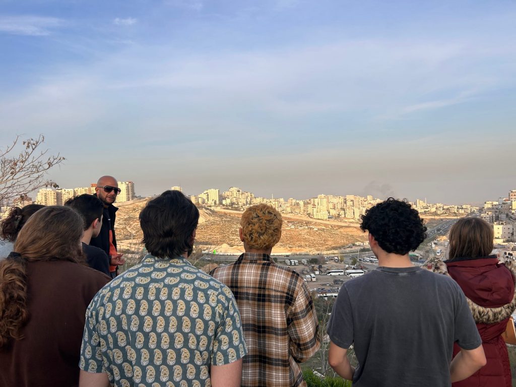 A group of students listen to a speaker in an outdoor setting.