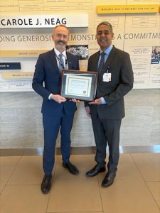 Two men in suits standing together holding a plaque