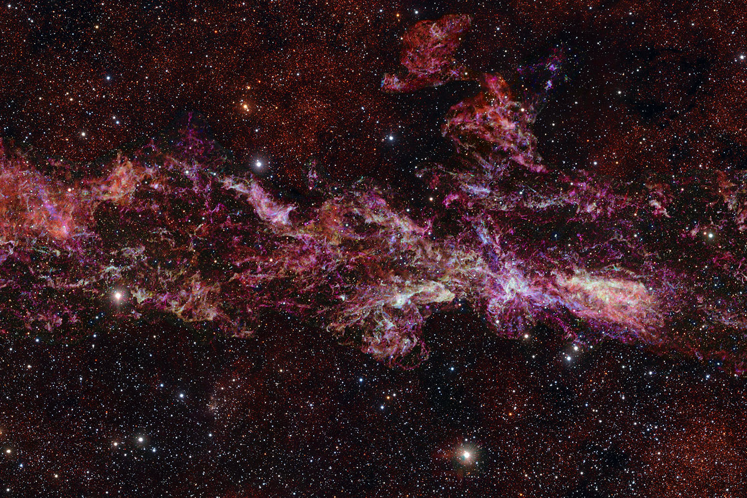 A view of the Milky Way, showing dense pink, red, and white clusters of stars.