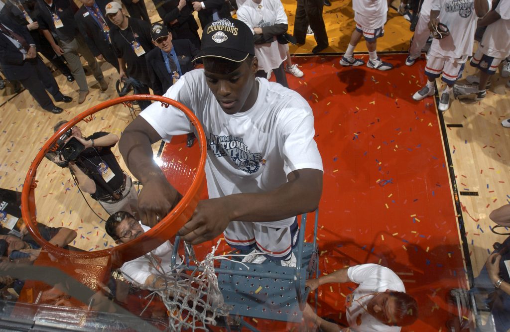 Emeka Okafor stands on a ladder and cuts down a basketball net.