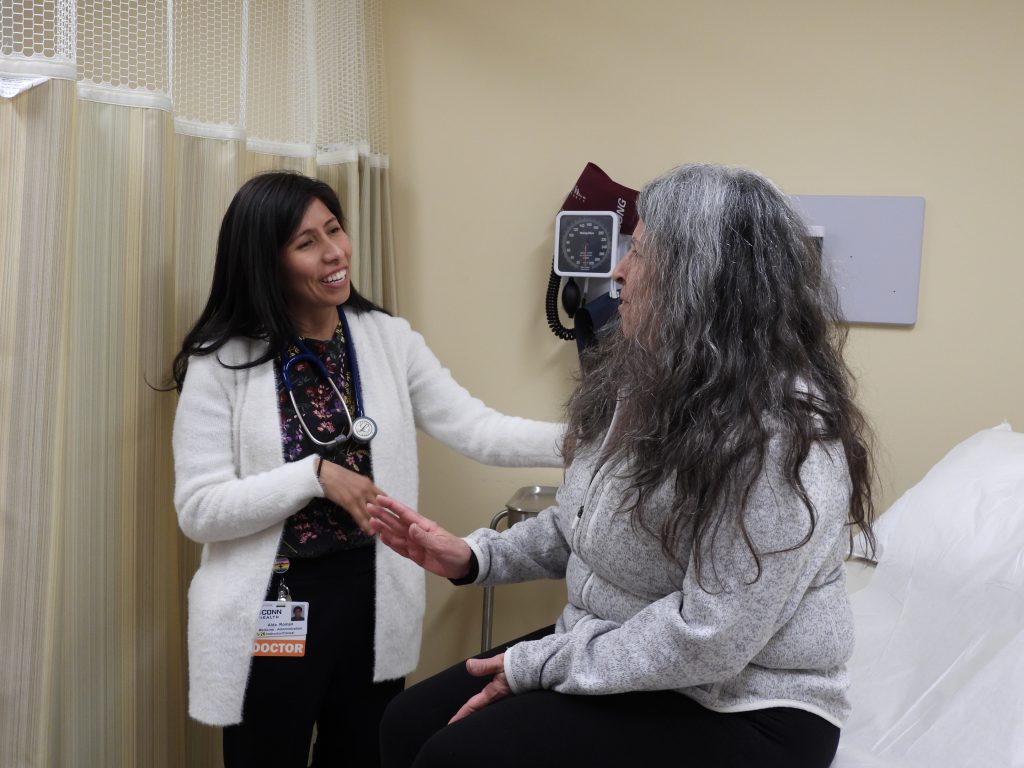 Dr. Aida Roman caring for primary care patient Denise L. Donnelly in exam room happily.