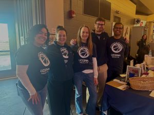 3 women and 2 men stand together in shirts with basketballs on them. 