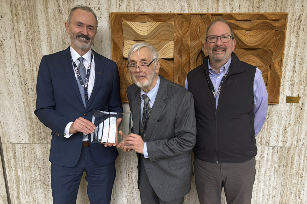 Three men stand together with a plaque