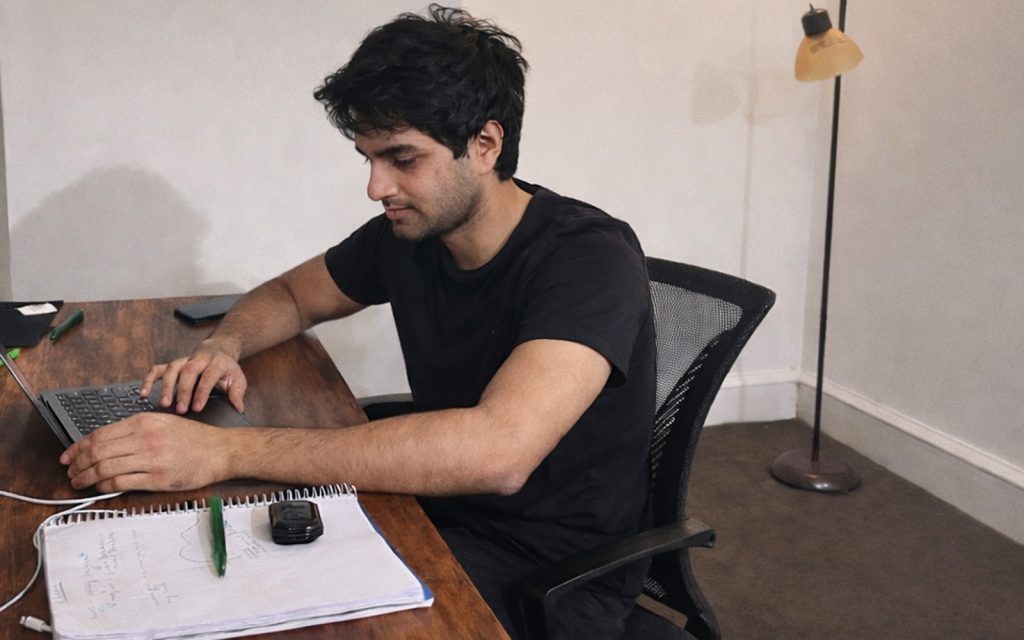 Uday Pandey, working on a laptop at a desk with a notebook beside him.