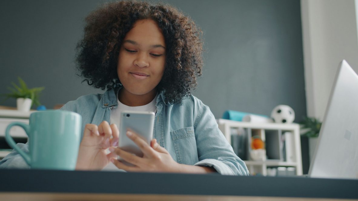 A young woman in an office smiles confidently at her smartphone