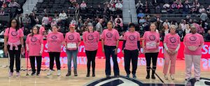 ten women standing on a basketball court wearing pink shirts