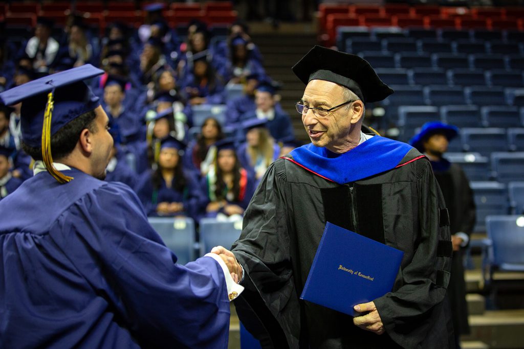 Andy Moiseff shakes a student’s hand while holding a diploma during commencement.